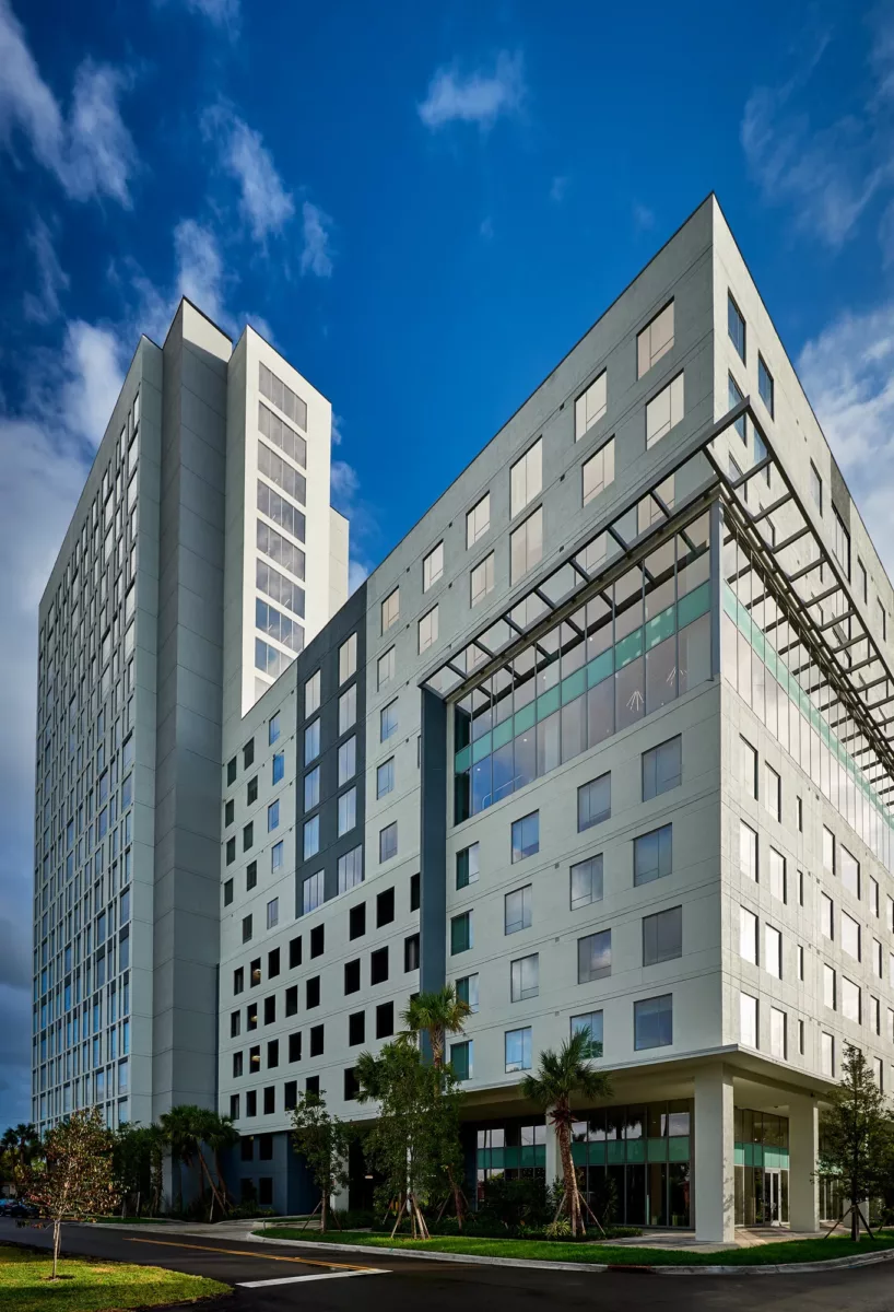 Modern high‑rise apartment building with glass accents, ground‑level entrance, and blue sky.