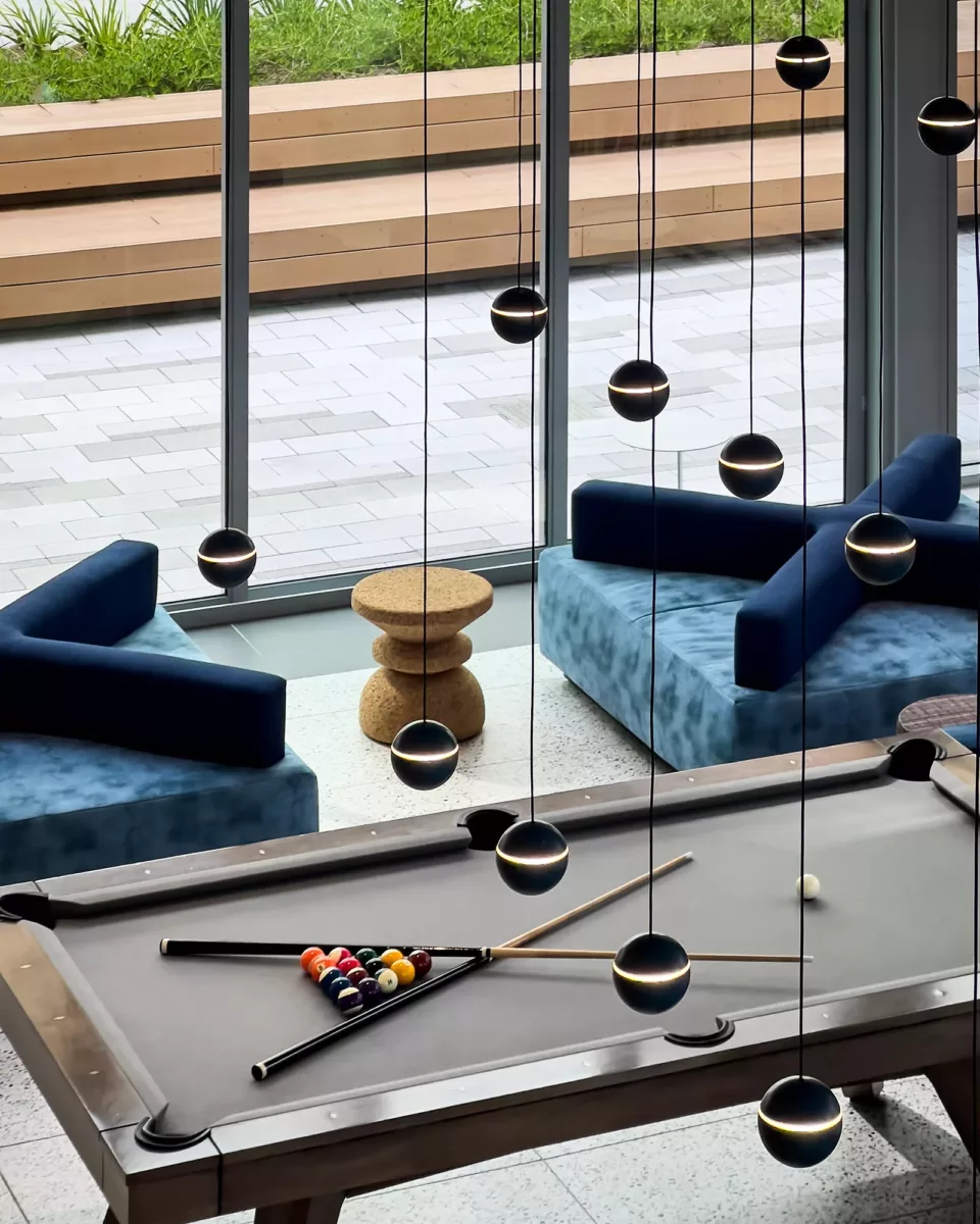 Billiards lounge with modern lighting, blue sofas, and floor‑to‑ceiling windows.