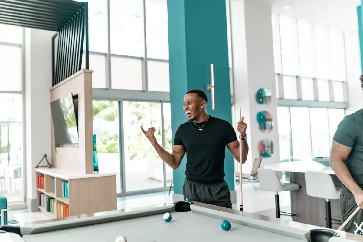 Resident playing pool in a bright game room with modern furnishings and high ceilings.