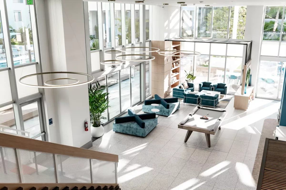 Two-story resident lounge with pool table, teal seating, and large windows