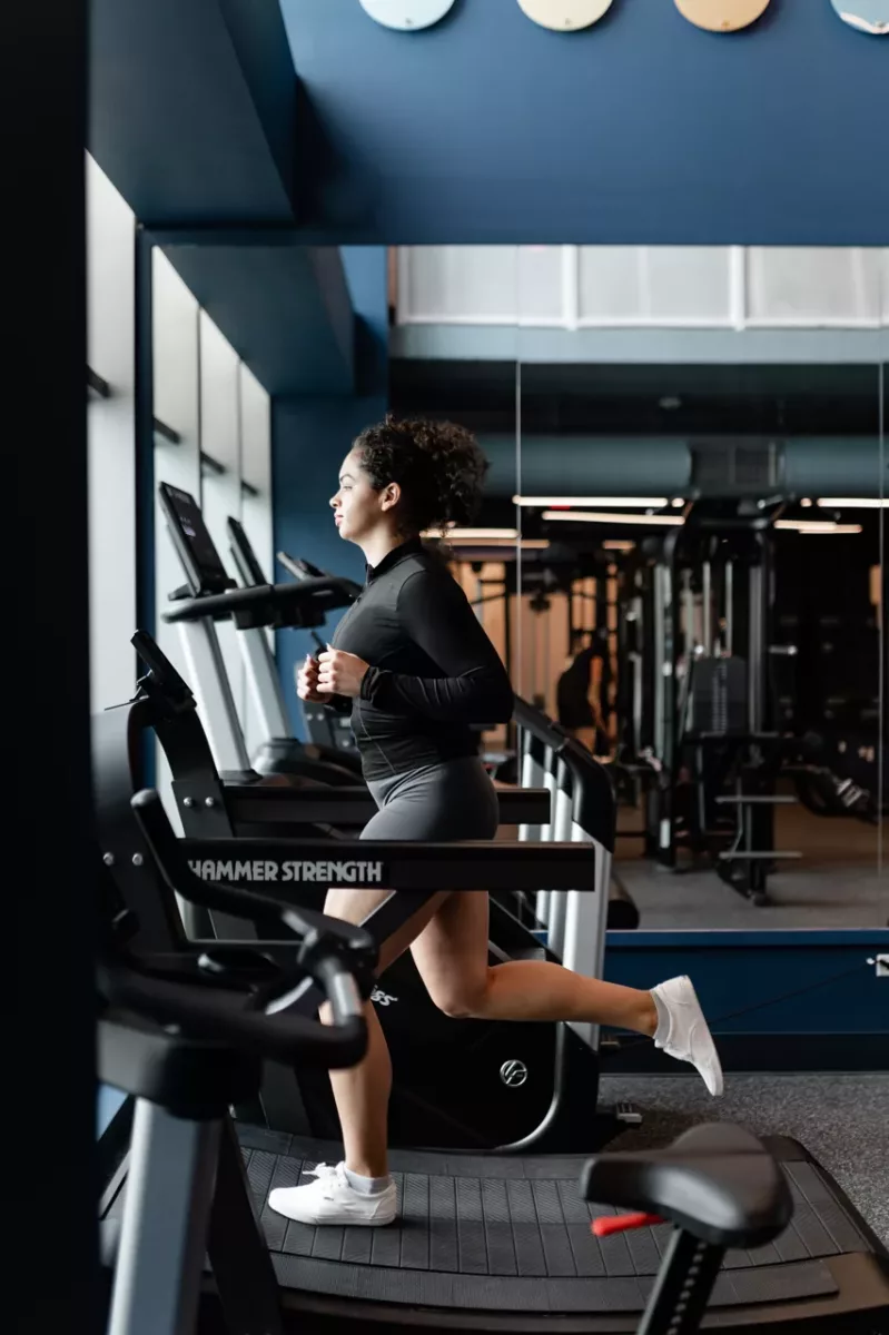 Resident running on a treadmill in a modern fitness center with mirrors and equipment.