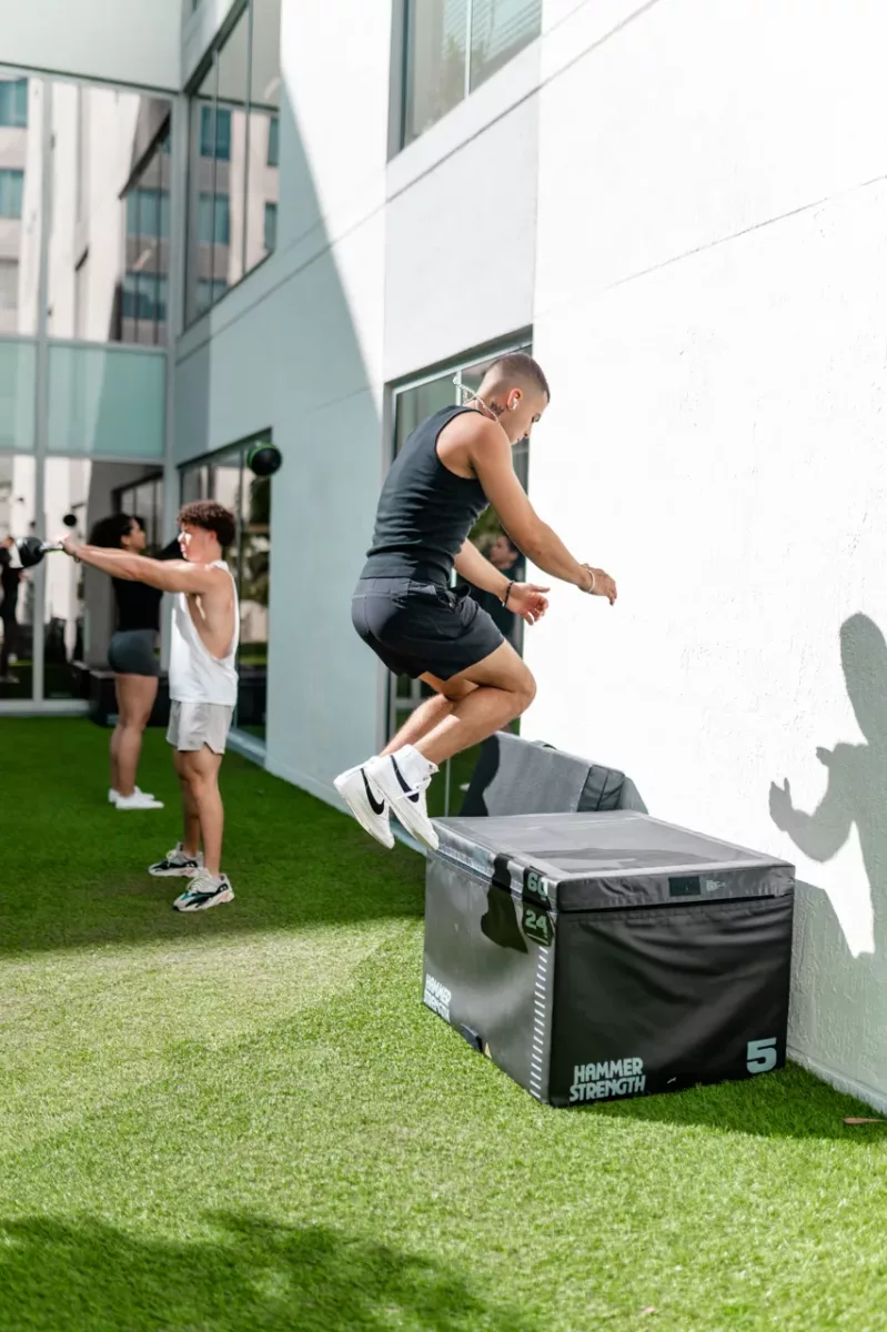 Residents exercising outdoors using plyometric box and fitness equipment on turf.