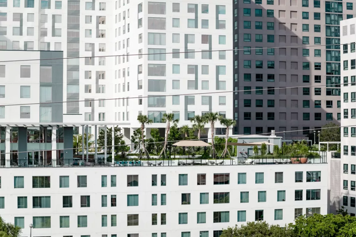 Close view of apartment buildings with elevated amenity deck, palm trees, and seating areas.