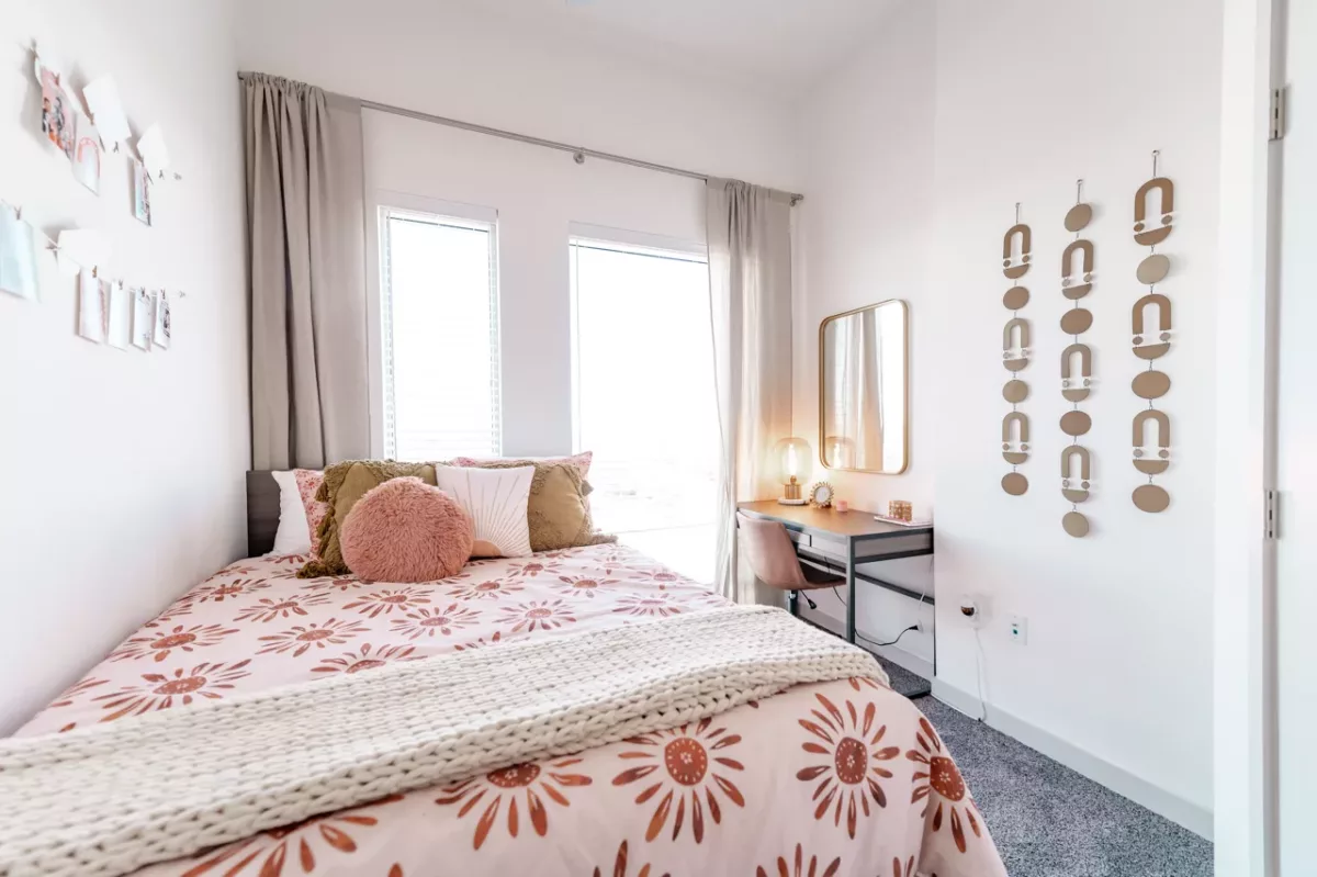 Bright bedroom with patterned bedding, desk vanity, mirror, and wall decor