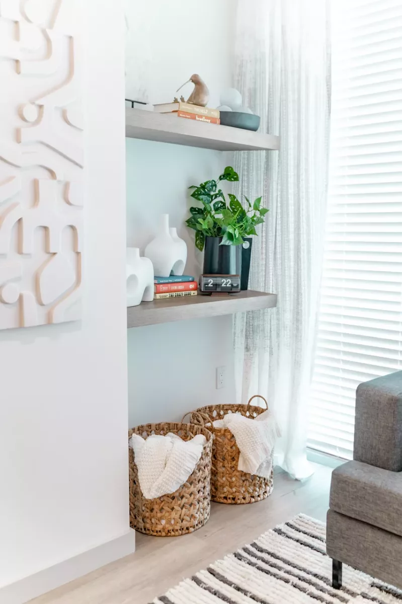 Floating shelves with decor and plant above woven baskets beside sunlit window