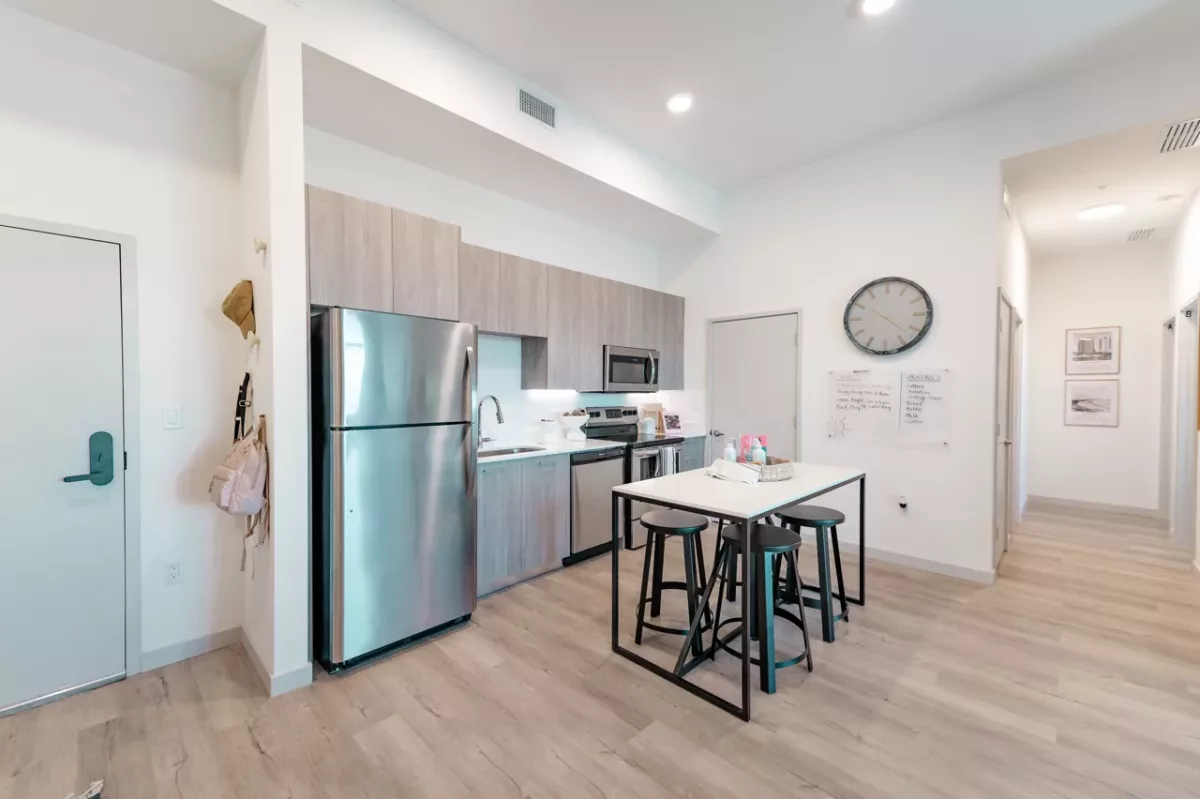Open kitchen with stainless steel appliances, island table, stools, and light wood flooring