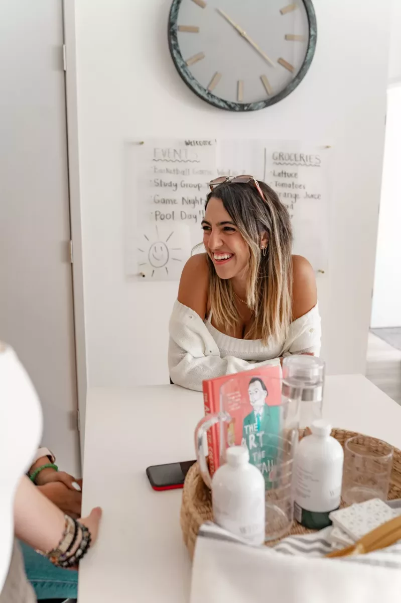 Resident seated at a communal table with books, décor items, and a wall clock behind.