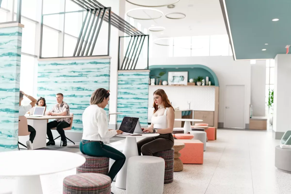 Residents working on laptops in a modern coworking lounge with café seating.